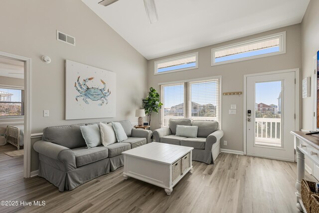 living area featuring visible vents, light wood-style floors, a healthy amount of sunlight, radiator heating unit, and high vaulted ceiling