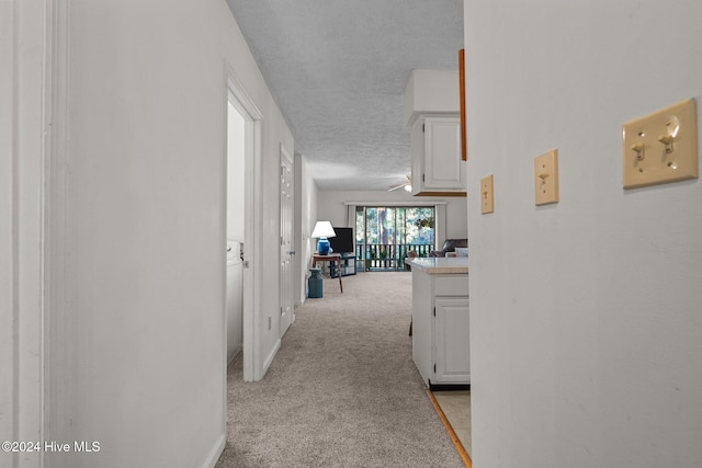 corridor with baseboards, light colored carpet, and a textured ceiling