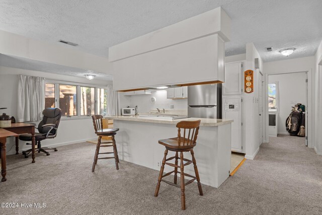 kitchen with light colored carpet, light countertops, a breakfast bar, and freestanding refrigerator