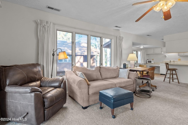 living room featuring a textured ceiling, visible vents, a ceiling fan, and light carpet