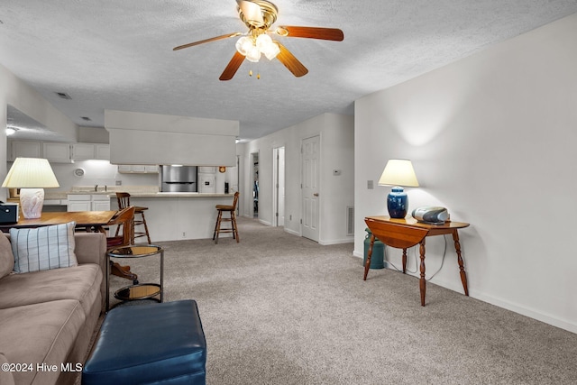 living area with baseboards, a textured ceiling, a ceiling fan, and light carpet