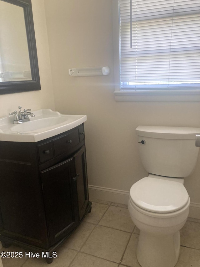 half bathroom with vanity, baseboards, toilet, and tile patterned floors