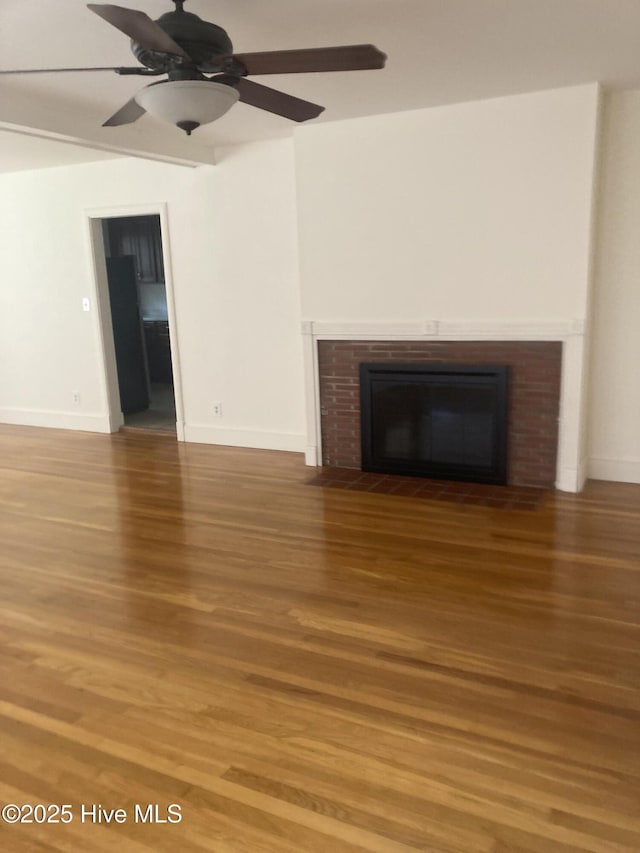 unfurnished living room featuring wood finished floors, a brick fireplace, ceiling fan, and baseboards