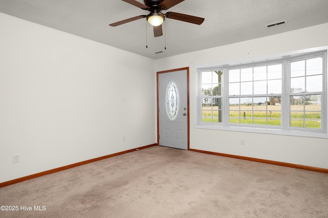 empty room with baseboards, a textured ceiling, a ceiling fan, carpet floors, and visible vents