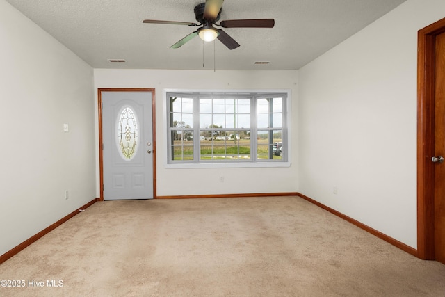 carpeted foyer entrance featuring a textured ceiling, ceiling fan, baseboards, and visible vents