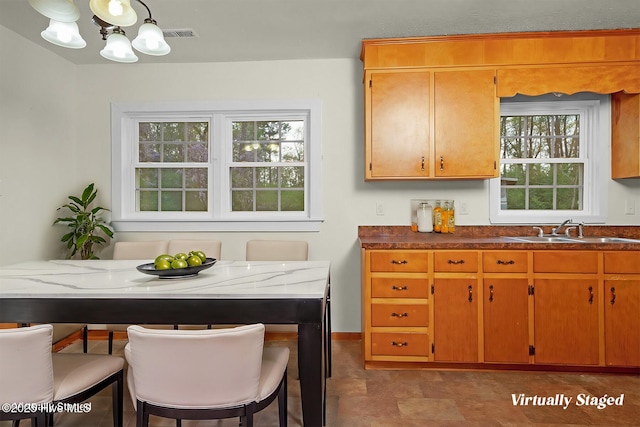 kitchen with a kitchen breakfast bar, brown cabinetry, a chandelier, a sink, and baseboards