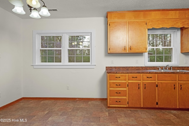 kitchen featuring dark countertops, a sink, baseboards, and a notable chandelier