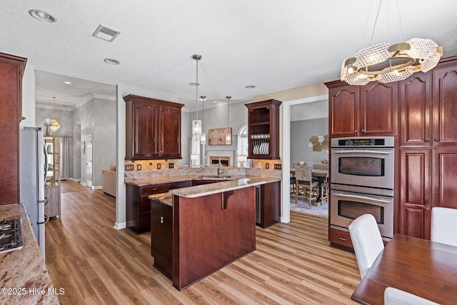 1096 Rutledge Ct NW, Calabash, NC 28467 - kitchen with stainless steel appliances, a fireplace, light wood-type flooring, a center island, and a chandelier