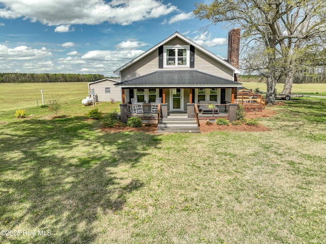 view of front of home with metal roof, a chimney, a porch, and a front yard