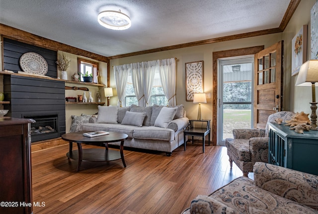 living room featuring a textured ceiling, wood finished floors, a large fireplace, and ornamental molding