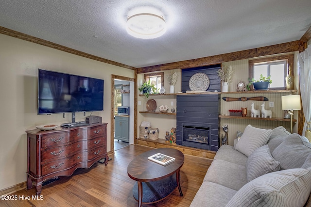 living area featuring crown molding, baseboards, a textured ceiling, a large fireplace, and wood finished floors