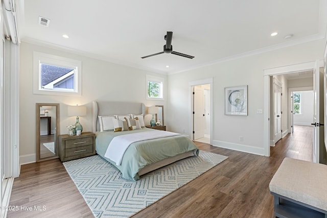 bedroom with baseboards, visible vents, crown molding, and wood finished floors