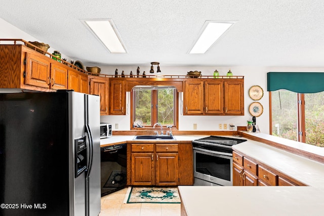 kitchen featuring a textured ceiling, a sink, light countertops, black appliances, and brown cabinetry