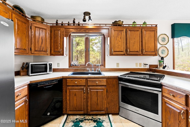kitchen with appliances with stainless steel finishes, a healthy amount of sunlight, brown cabinetry, and a sink