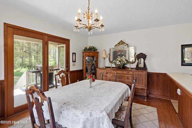dining room featuring light wood-style flooring, a chandelier, a textured ceiling, a wainscoted wall, and wooden walls