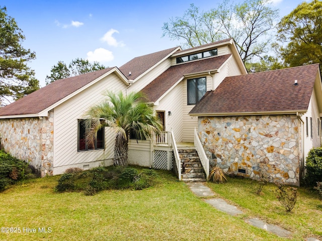 back of property with a yard, stone siding, and a shingled roof
