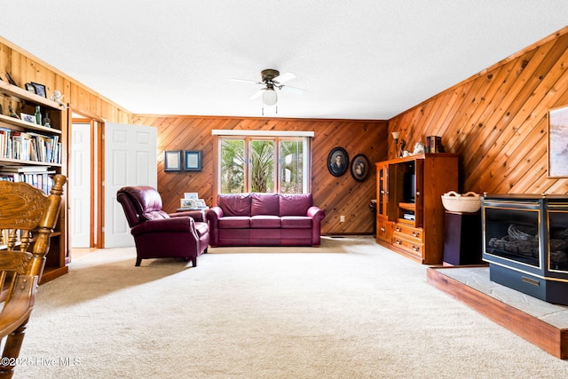 living room with wood walls, carpet, a ceiling fan, and a textured ceiling