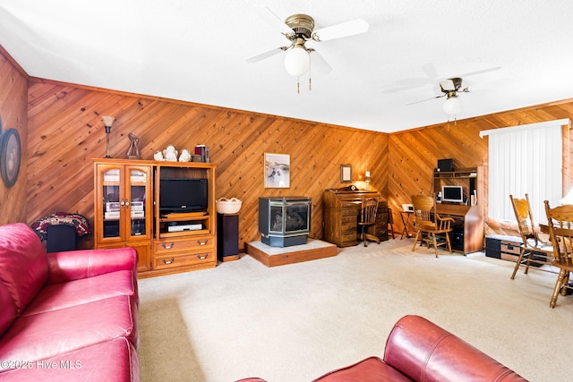 living room with carpet flooring, wooden walls, ceiling fan, and a wood stove
