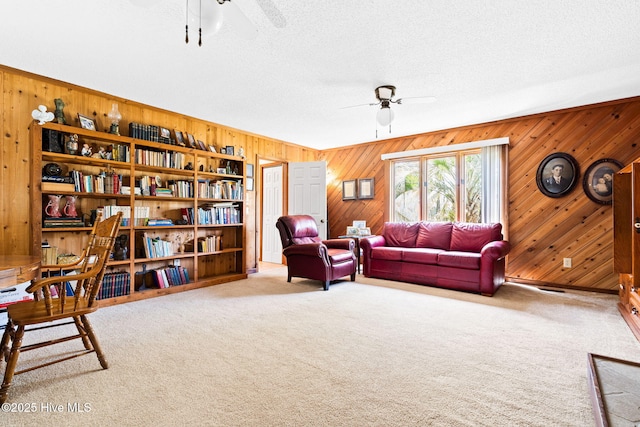 interior space featuring wood walls, a ceiling fan, a textured ceiling, and carpet