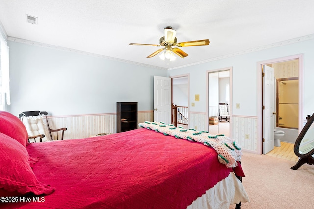 carpeted bedroom featuring crown molding, a wainscoted wall, visible vents, and ensuite bath