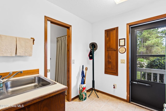 interior space with light tile patterned floors, a textured ceiling, a sink, and baseboards