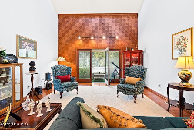 living area with wood finished floors, wooden walls, and a towering ceiling
