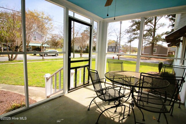 sunroom featuring a residential view, a wealth of natural light, outdoor dining area, and ceiling fan