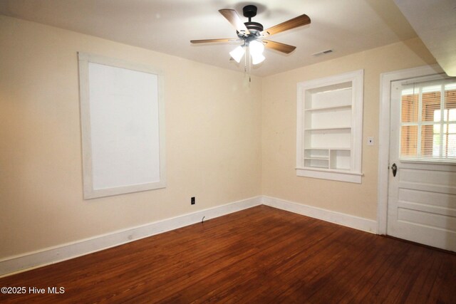 unfurnished room with baseboards, visible vents, built in shelves, and dark wood finished floors