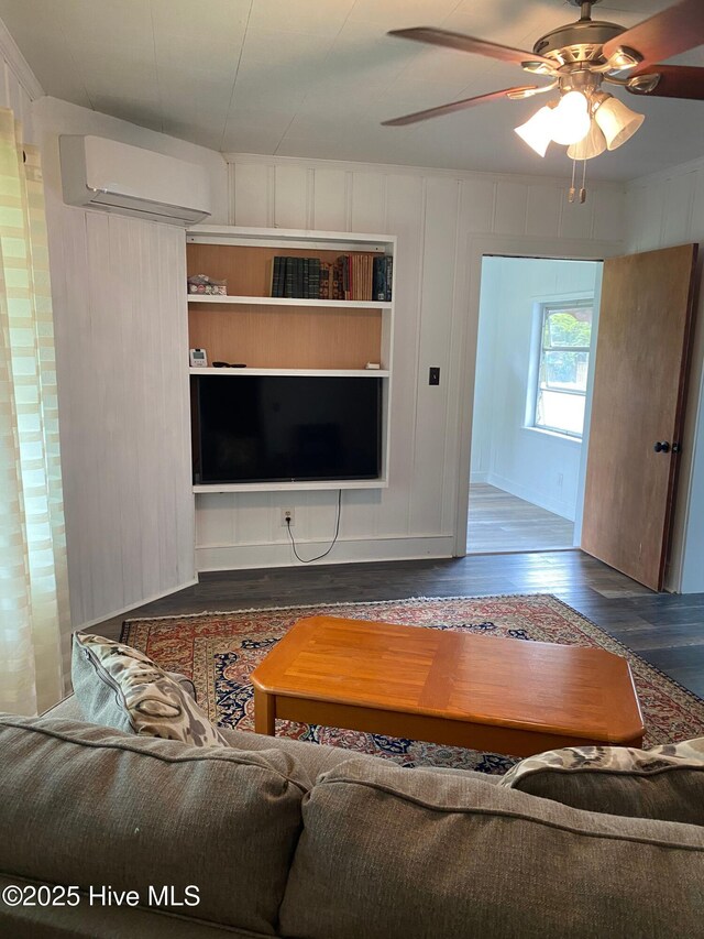 living area featuring ceiling fan, wood finished floors, an AC wall unit, and a decorative wall