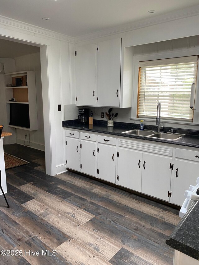 kitchen with ornamental molding, dark wood-type flooring, a sink, dark countertops, and white cabinets