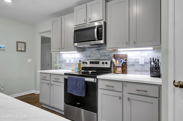 kitchen featuring tasteful backsplash, baseboards, dark wood-style floors, light stone countertops, and appliances with stainless steel finishes