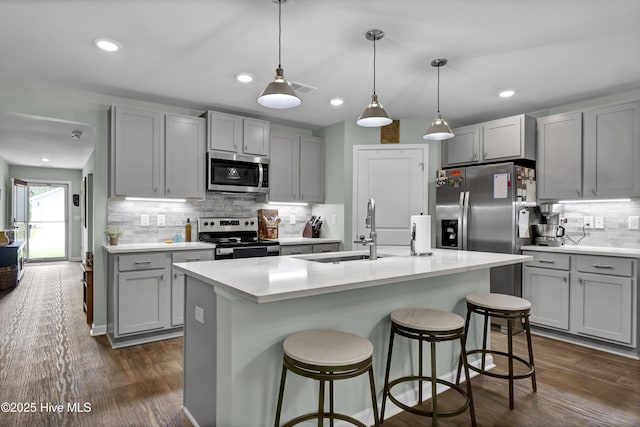 kitchen featuring dark wood finished floors, appliances with stainless steel finishes, a sink, gray cabinets, and a kitchen breakfast bar