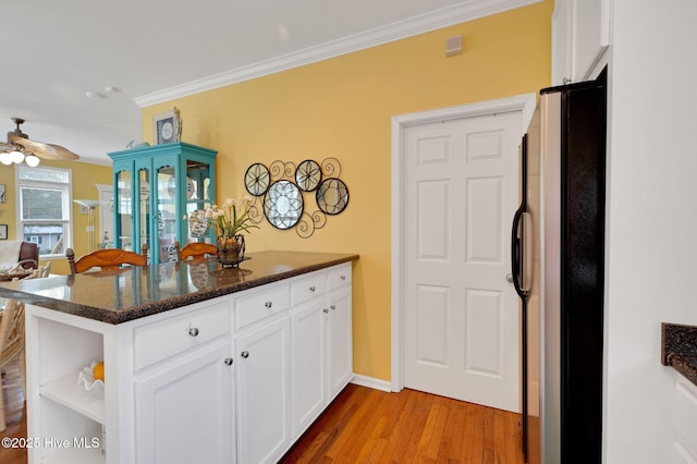 kitchen featuring freestanding refrigerator, white cabinetry, wood finished floors, a peninsula, and ornamental molding
