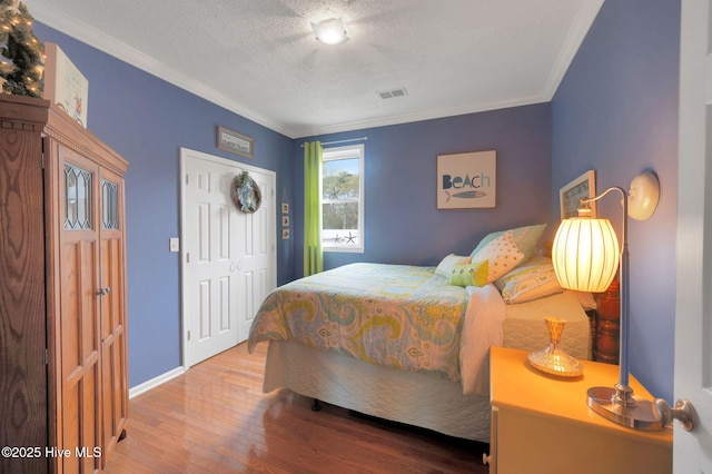 bedroom featuring a textured ceiling, visible vents, crown molding, baseboards, and wood-type flooring
