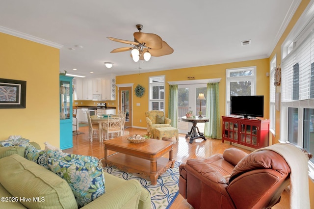 living room featuring crown molding, a ceiling fan, baseboards, visible vents, and light wood-style floors
