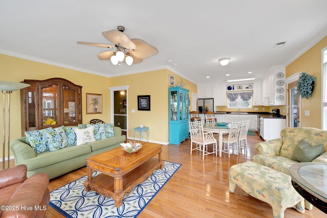 living room with visible vents, crown molding, ceiling fan, and light wood-type flooring