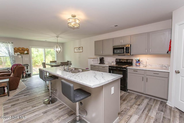 kitchen with a sink, stainless steel microwave, gray cabinetry, electric range, and a breakfast bar area