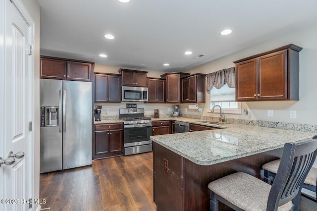 kitchen featuring appliances with stainless steel finishes, a sink, a peninsula, dark wood finished floors, and dark brown cabinets