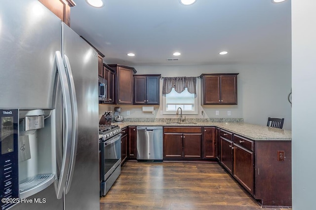 kitchen with appliances with stainless steel finishes, a sink, light stone countertops, a peninsula, and dark wood-style floors