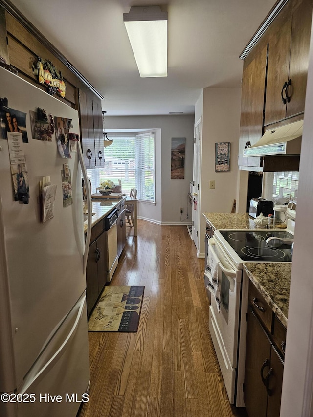 kitchen with wood finished floors, dark brown cabinets, baseboards, under cabinet range hood, and white appliances