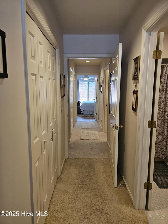 hallway featuring baseboards and light carpet