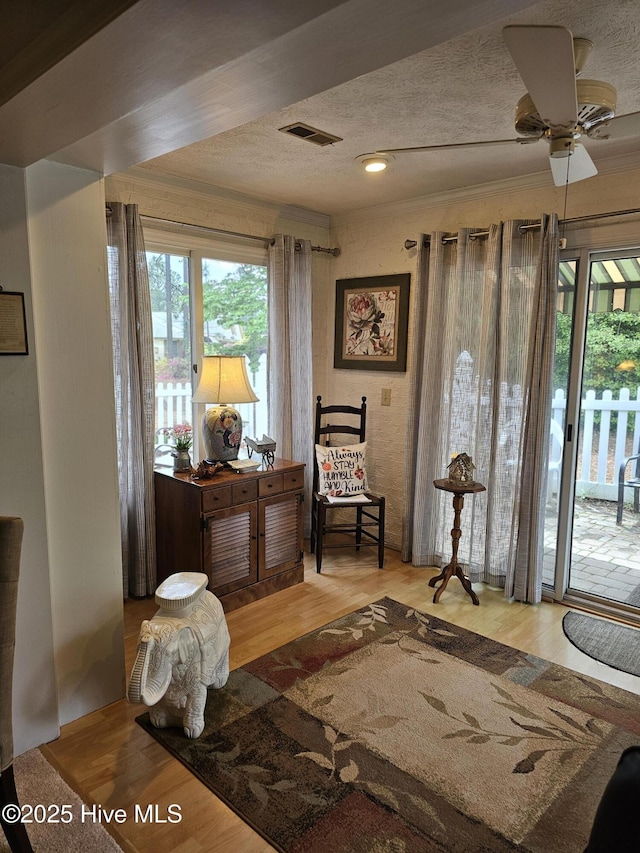 sitting room with wood finished floors, a ceiling fan, a textured ceiling, and visible vents
