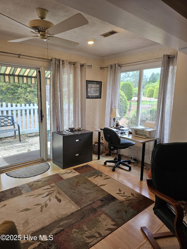 office area with a textured ceiling, a ceiling fan, wood finished floors, visible vents, and ornamental molding