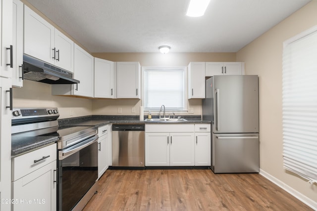 1507 Brookfield Rd, Rockingham, NC 28379 - kitchen featuring appliances with stainless steel finishes, under cabinet range hood, dark countertops, white cabinets, and light wood-style flooring