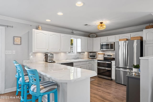 kitchen with a kitchen bar, a peninsula, white cabinets, a sink, and stainless steel appliances
