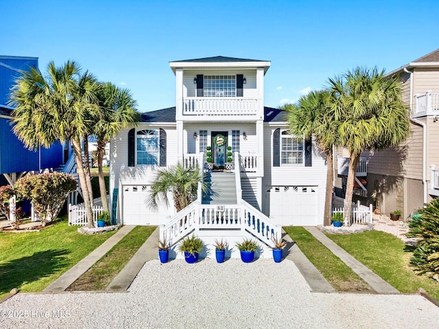 coastal inspired home with stairway, driveway, a front yard, a garage, and covered porch