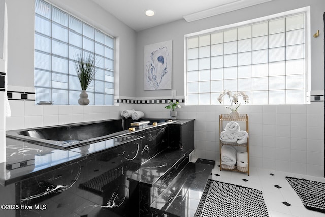 bathroom featuring a bath, a healthy amount of sunlight, tile patterned flooring, and tile walls