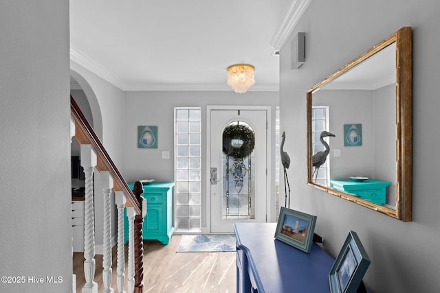 entrance foyer with arched walkways, stairway, crown molding, and wood finished floors