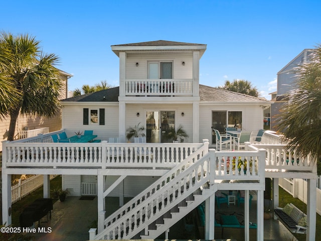 rear view of property featuring a shingled roof, stairway, and a balcony