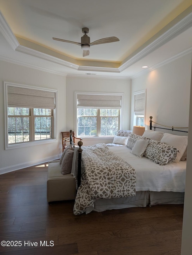 bedroom featuring a raised ceiling, ornamental molding, dark wood-style flooring, baseboards, and ceiling fan